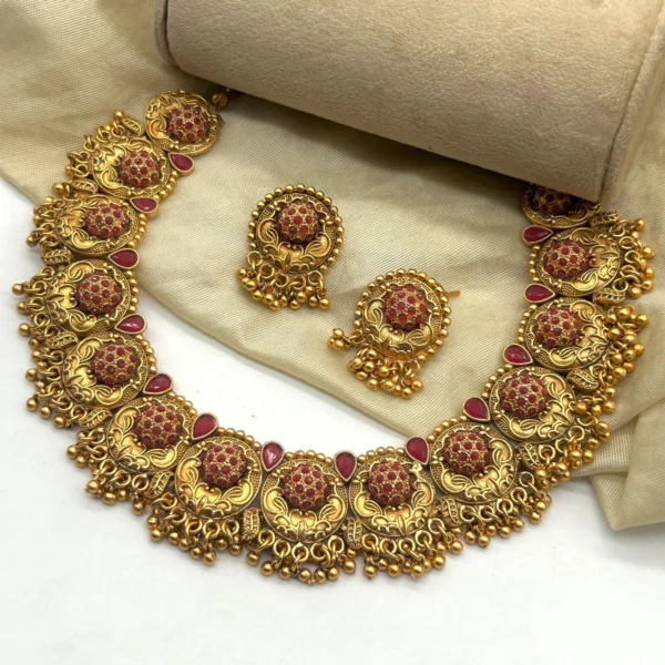 Gold plated South Indian choker necklace set with earrings featuring red stones and temple jewelry design.
